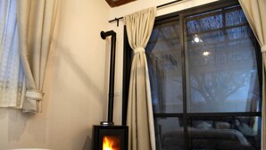 Ett mysigt rum med en vedeldad kamin, ett fönster med gardiner och utsikt över naturen.