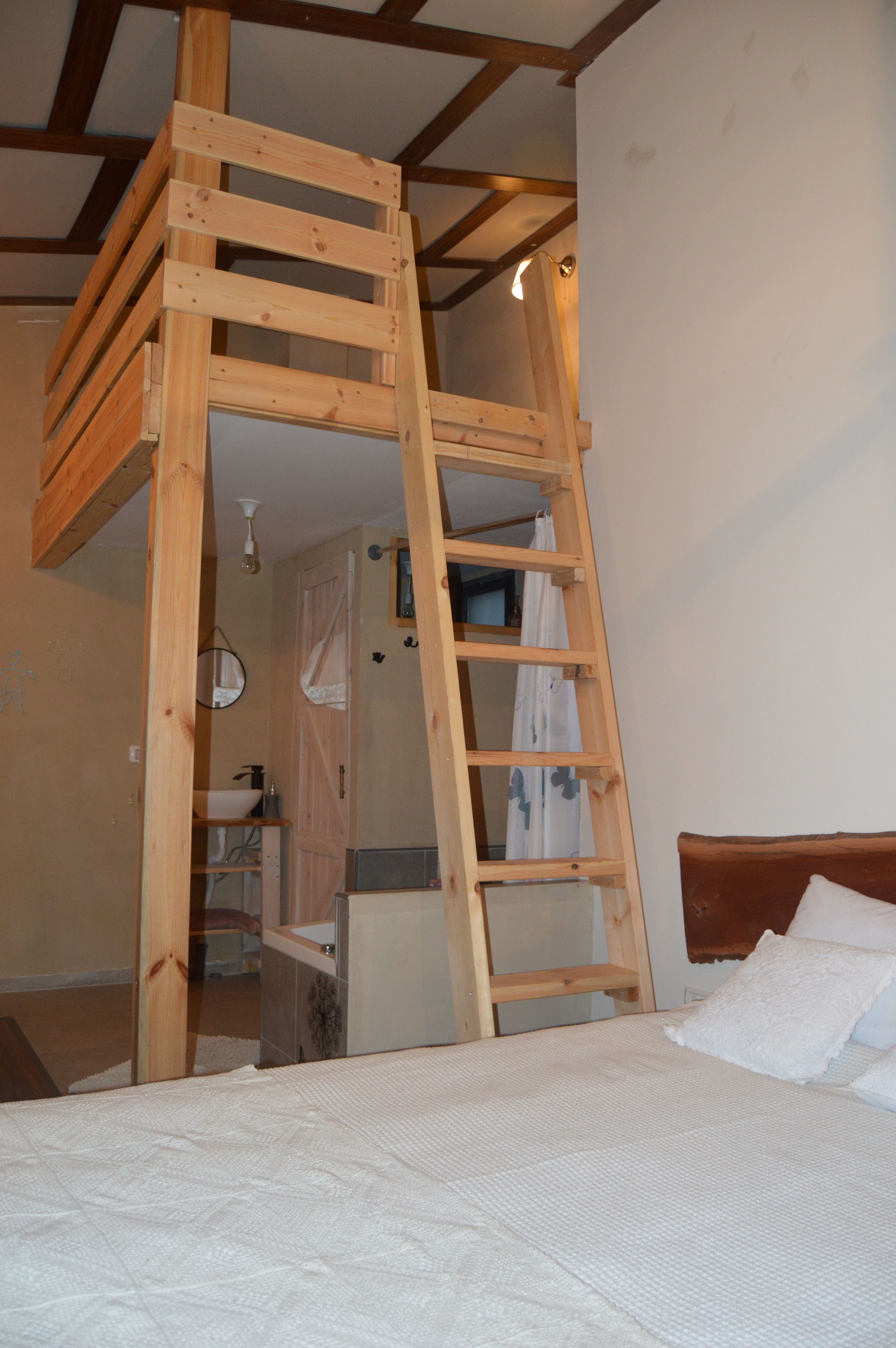Eine Holzleiter ist an einem Etagenbett in einem Zimmer befestigt, das ein weißes Bettlaken und ein Holz-Kopfteil hat.