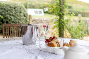 Une table dressée avec une bouteille de champagne, deux verres, un saladier de fraises et une carafe d’eau, le tout posé sur une nappe en dentelle.