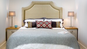 Un lit bien fait, agrémenté d’un coussin à motifs, deux tables de chevet avec des lampes et une petite table en bois sur laquelle se trouve une tasse.