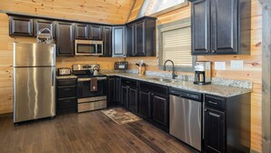 A modern kitchen with stainless steel appliances, dark cabinetry, and a granite countertop. -  Mt. LeConte Views! Cosy Luxury Cabin, Fire Pit, Hot Tub, Outdoor Pool, Location (Gatlinburg)