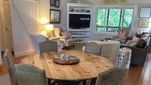 Un coin repas avec une table en bois, des chaises en osier, un téléviseur et un ventilateur de plafond.