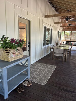 A covered porch with a table and chairs, a wicker basket with flowers, and a door leading inside.