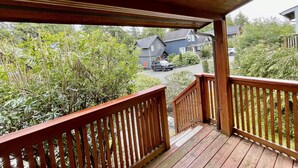 A wooden deck with a railing, overlooking a residential area with houses and a car parked on the street. - Great cabin near trails and beaches - 13T (Ucluelet)