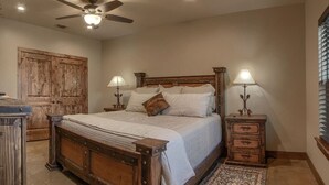 A bedroom with a wooden bed, two bedside tables with lamps, a ceiling fan, and a large wooden wardrobe.