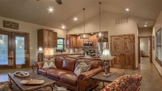 A spacious living room with a brown leather sofa, a coffee table, and a dining area with wooden cabinets and a kitchen in the background.