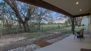 A covered patio with a view of a rural landscape, including trees and a fenced field.