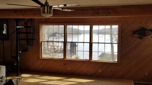 Una habitación con paredes de madera, un ventanal con vistas a un muelle y al agua, un ventilador de techo y una decoración de pez en la pared.