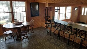 Un interior de madera con una mesa redonda para comer, varias sillas y una zona de cocina con mostrador.