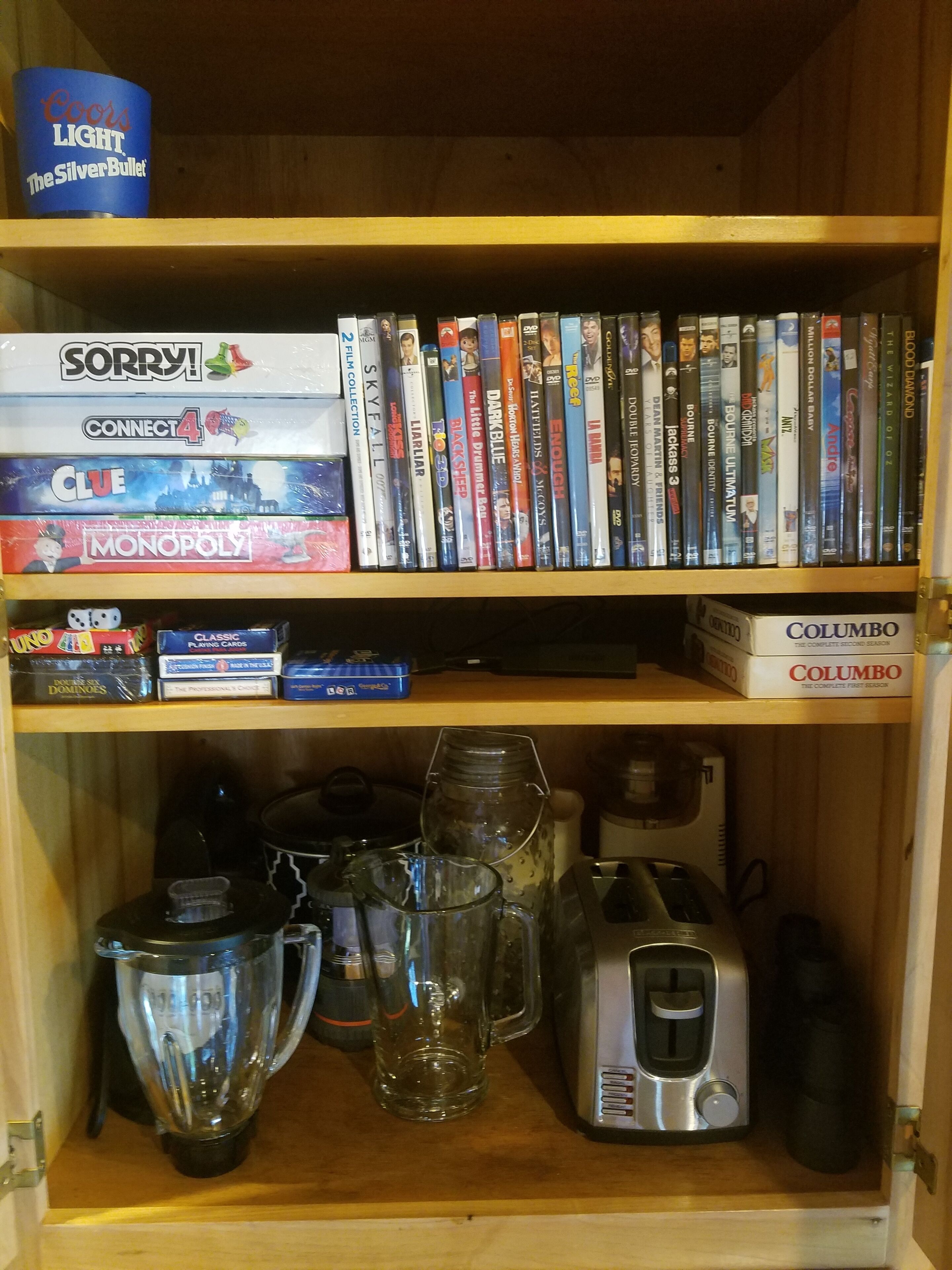 A wooden shelf with various board games, DVDs, and a coffee maker.