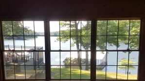 Una habitación con un amplio ventanal con vista a un lago, una terraza de madera y un área con césped.