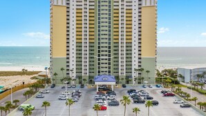 A multi-story hotel with a central entrance, parking lot, and beachfront view. - Luxury Beachfront Stay at Boardwalk – 2BR Condo w/ Balcony, Gulf Views & Free Perks (Panama City Beach)