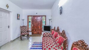 Una habitación con una puerta de madera, un televisor, un sofá estampado y una lámpara colgante roja.