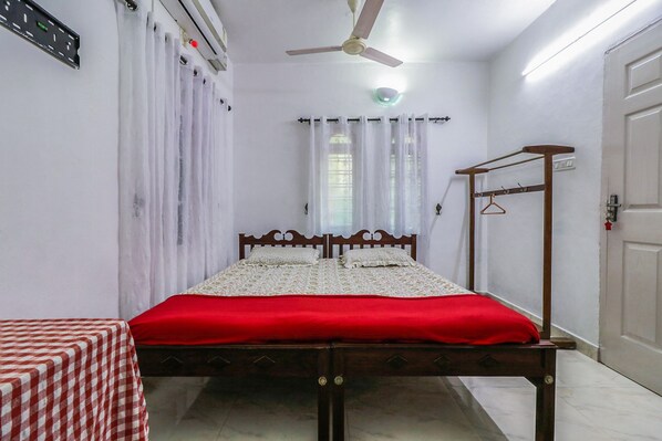 A bedroom with a bed, a table, a ceiling fan, a window with curtains, and a door.