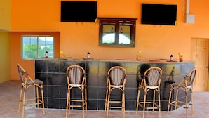 A bar area with a counter, five wicker chairs, a television, and a window with a view. - Takuma Boutique Hotel Rooms & Suites Jamaica  (Montego Bay)
