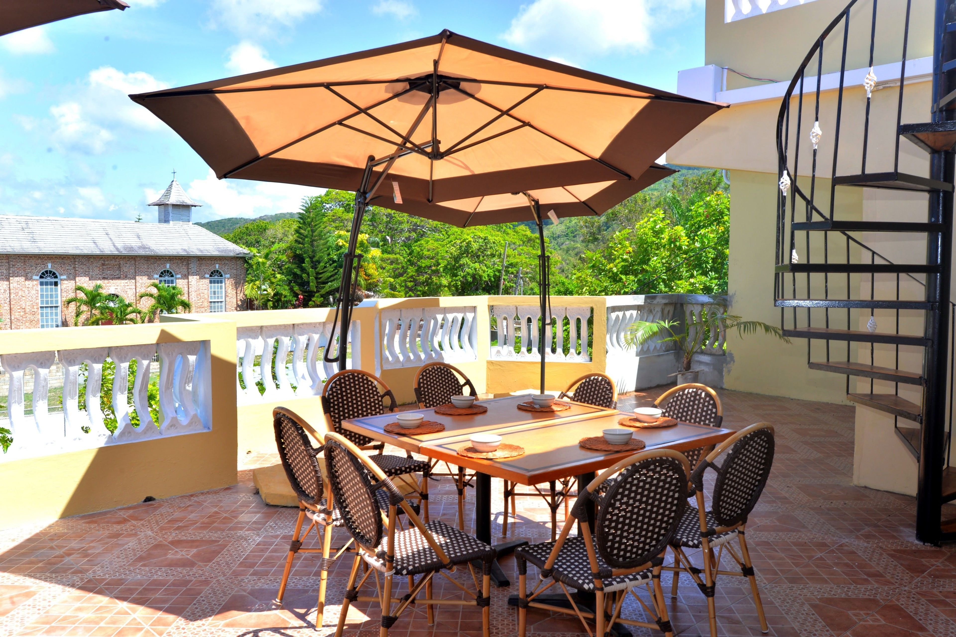 An outdoor patio with a table and chairs, surrounded by a white railing and potted plants.