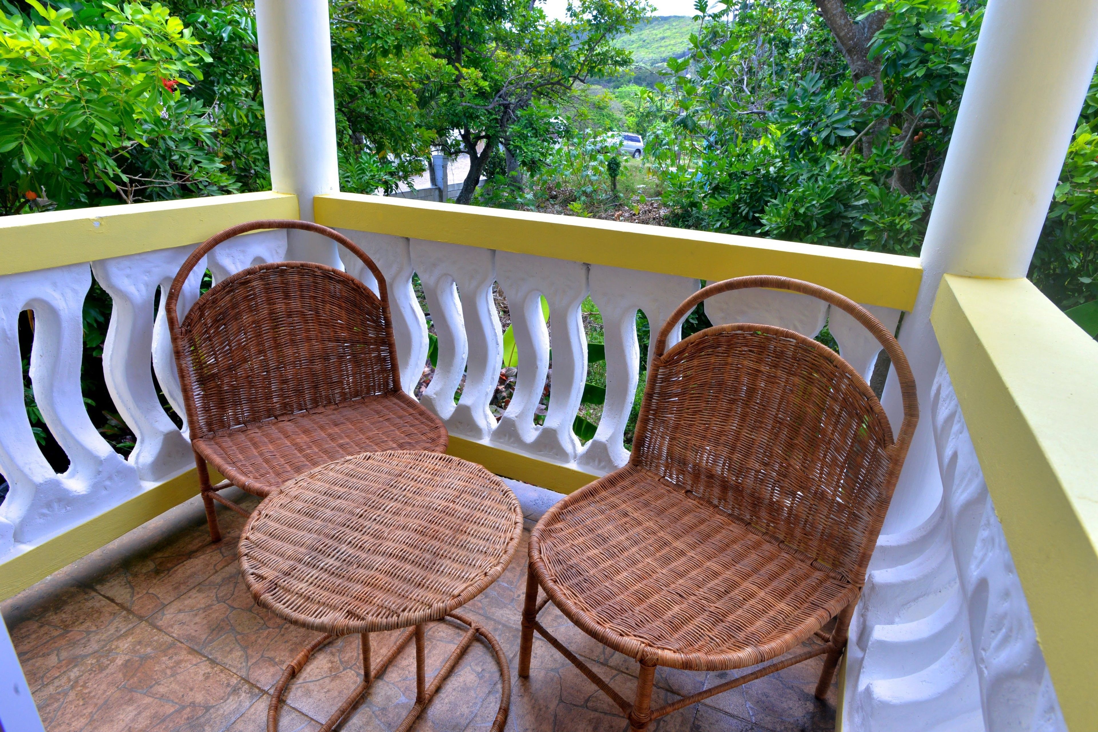 A balcony with wicker chairs and a small table, surrounded by a white railing with yellow accents.