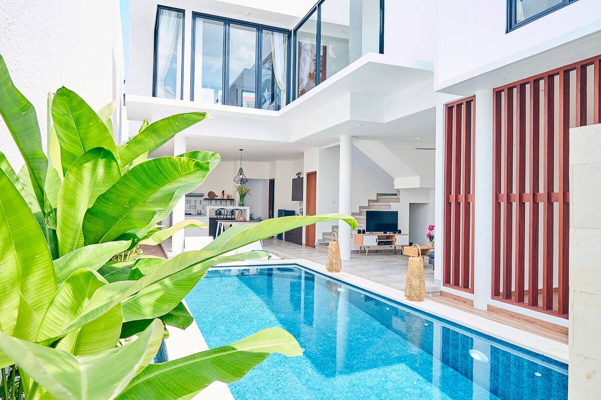 A modern pool area with a clear blue pool, surrounded by lush green plants.