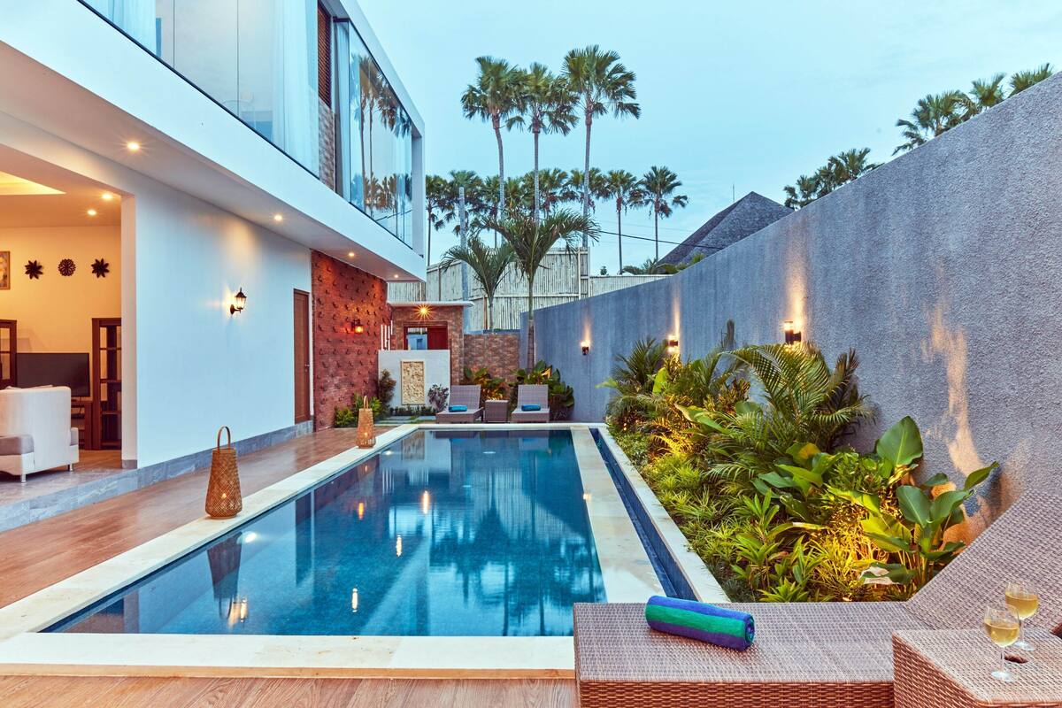 A modern pool area with lounge chairs, a small pool, and a stone wall with plants.