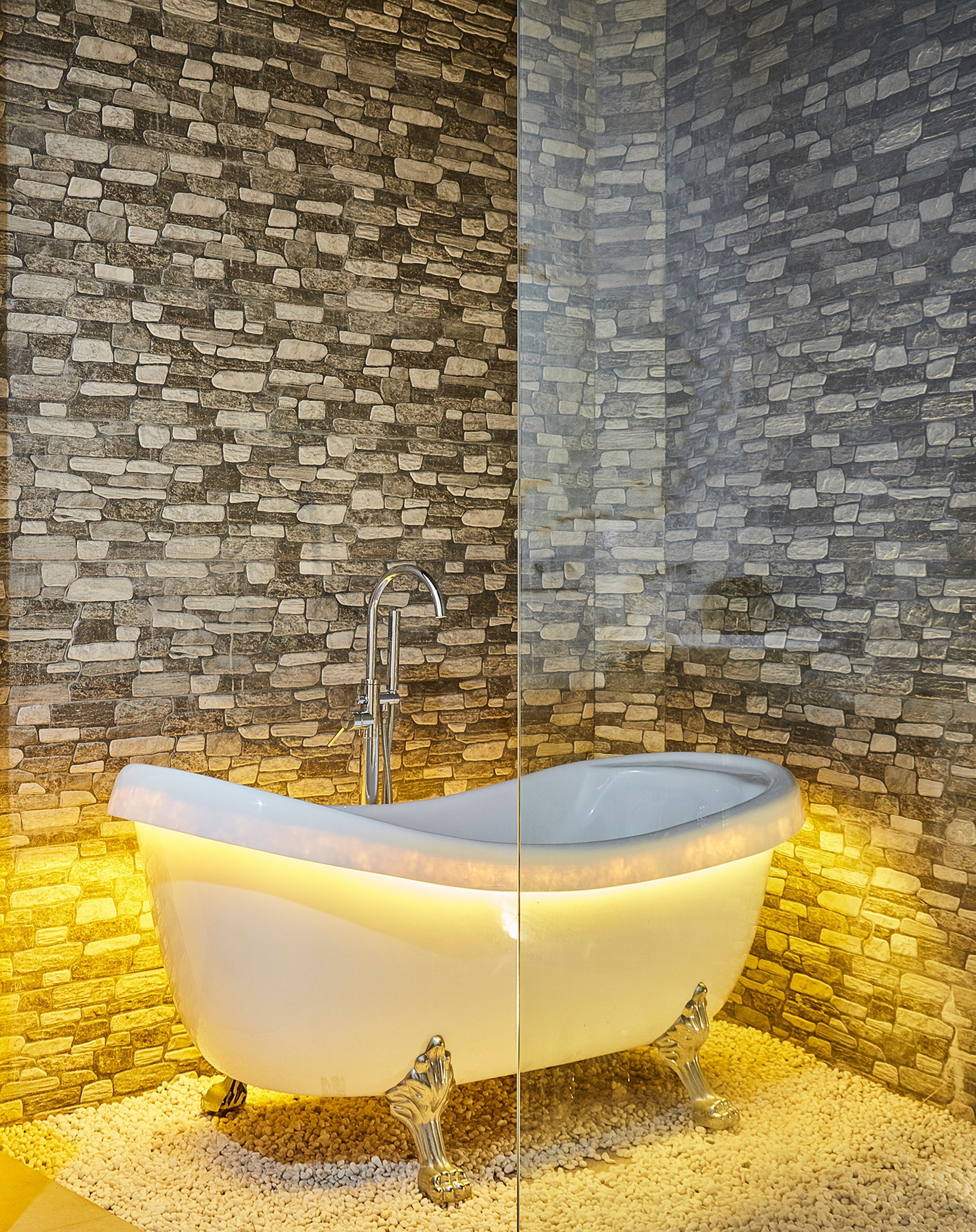 Une baignoire autoportante au design moderne, placée contre un mur en pierre à texture marquée.