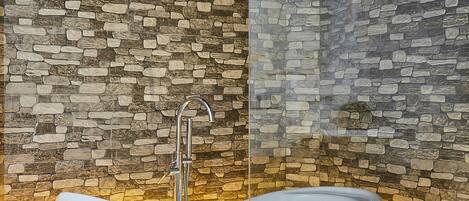 Une baignoire autoportante au design moderne, placée contre un mur en pierre à texture marquée.