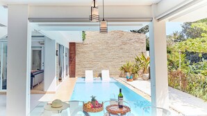 Un espace piscine extérieur moderne, agrémenté d’un mur en pierre, de sièges et d’une table avec une bouteille et des verres.