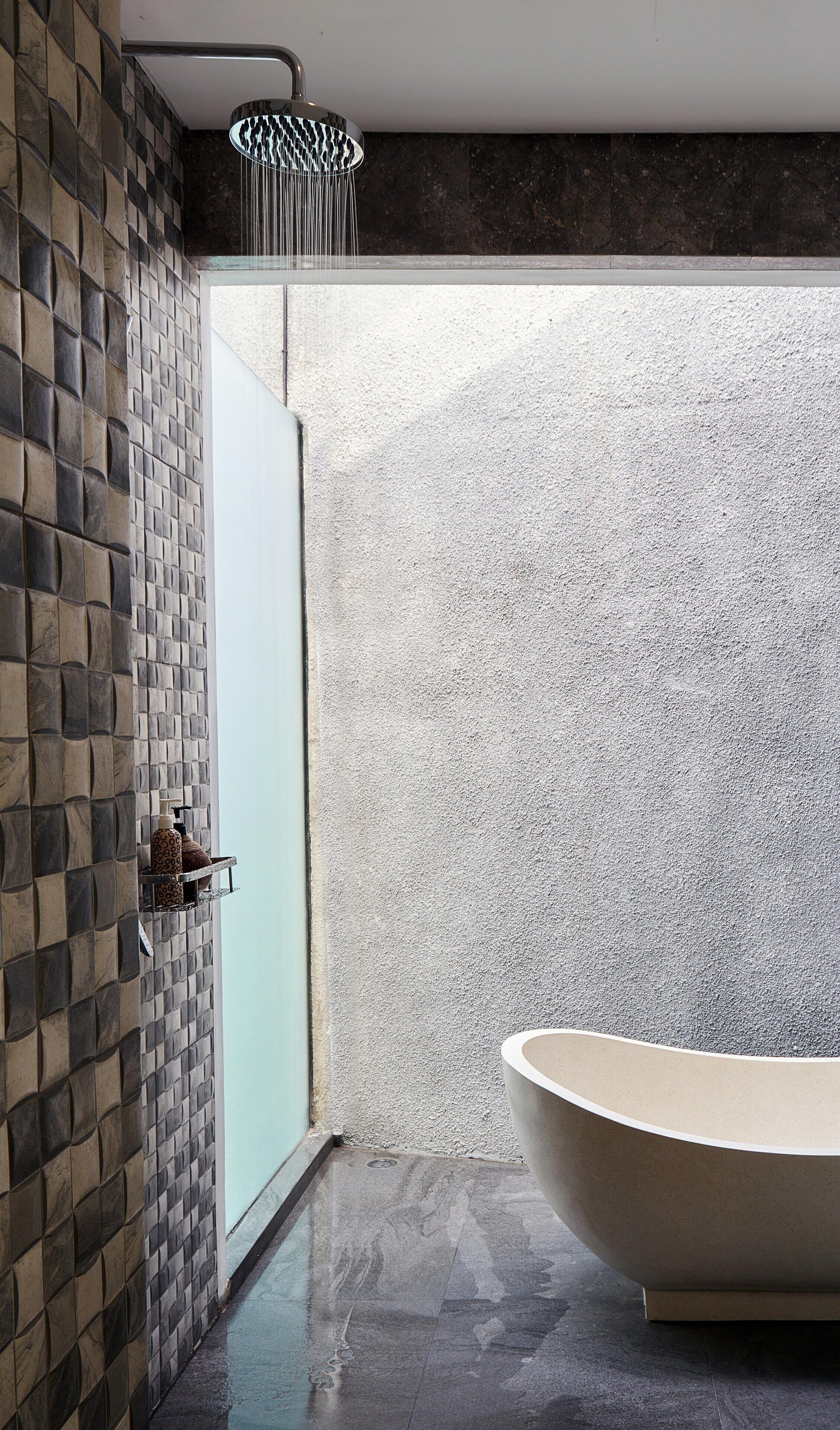 A modern bathroom with a freestanding bathtub, a shower with a unique light fixture, and a textured wall.