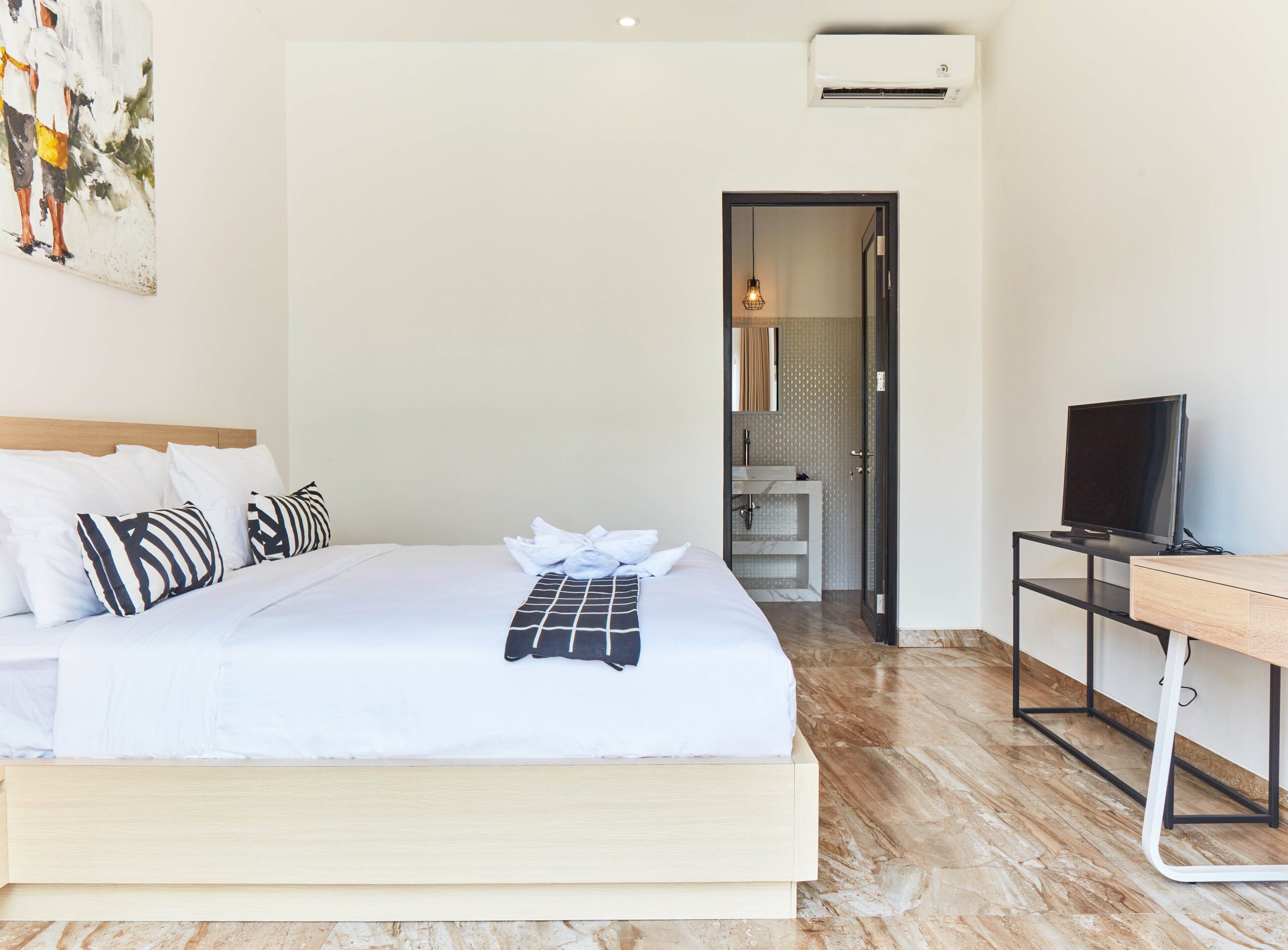 A hotel room with a bed, a TV, a desk, and a bathroom visible through an open door.
