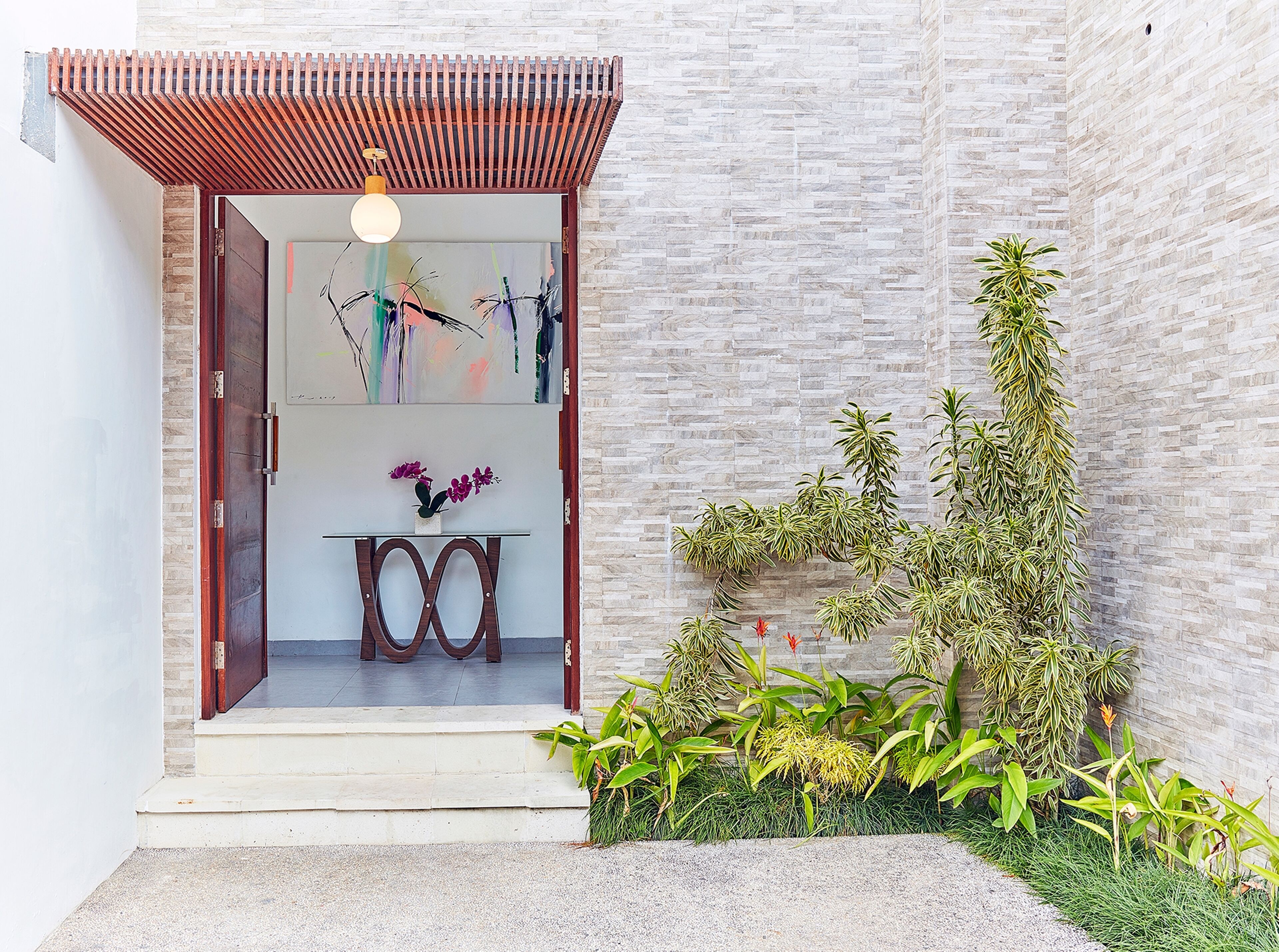 A modern entrance with a wooden door, a small table with purple flowers, and a variety of plants.