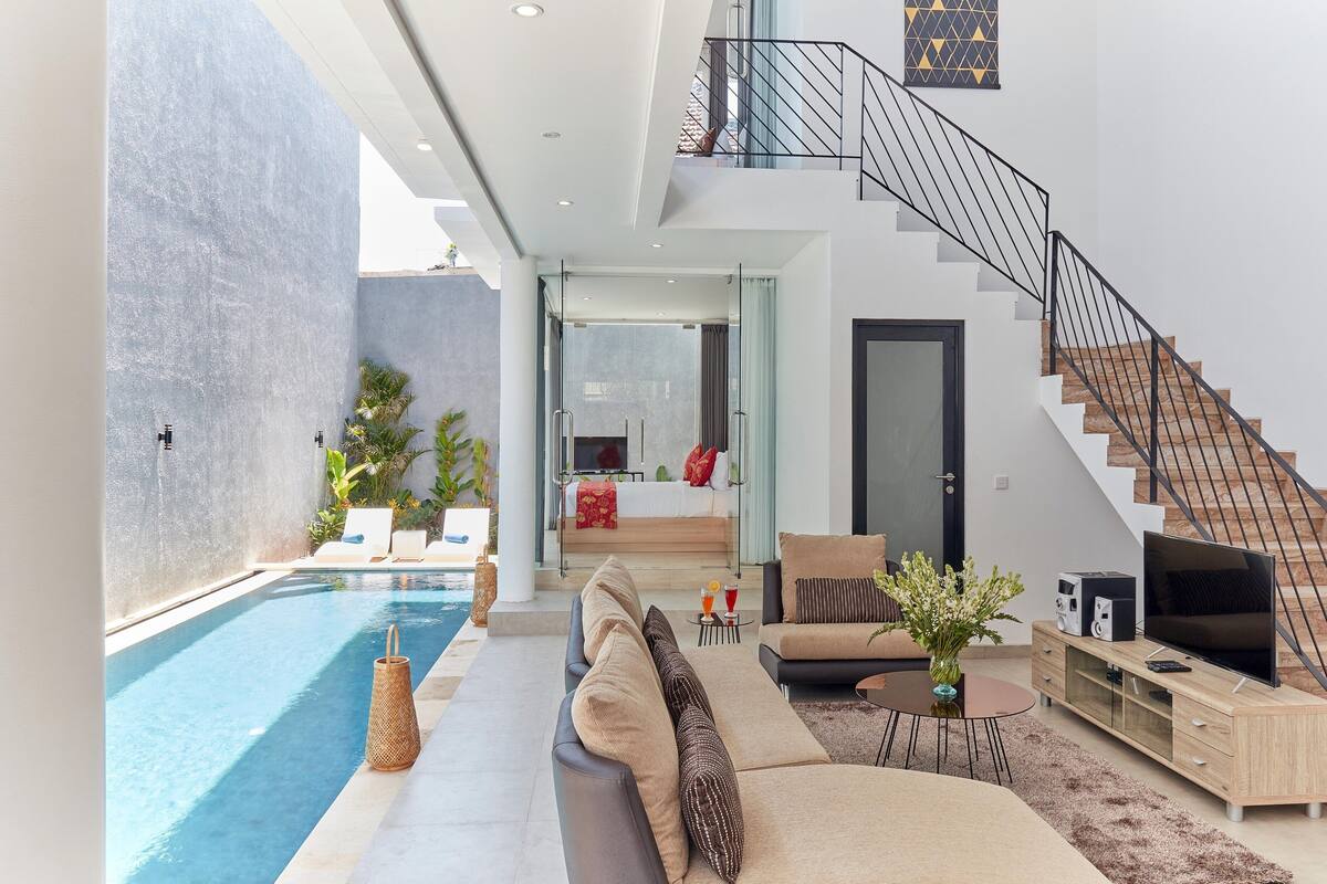 A modern living area with a pool, a sofa set, a TV, and a staircase.
