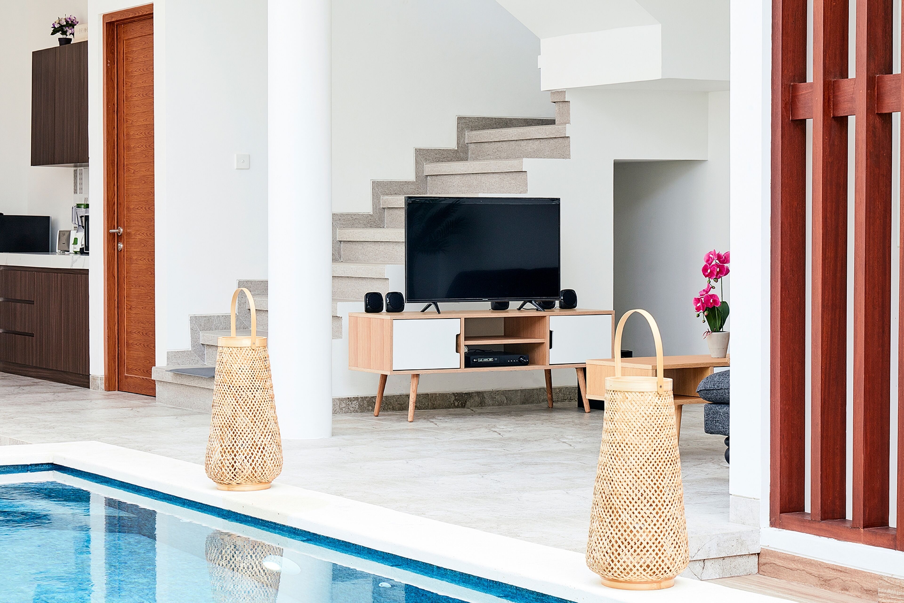A modern living room with a TV, wooden staircase, and a pool.
