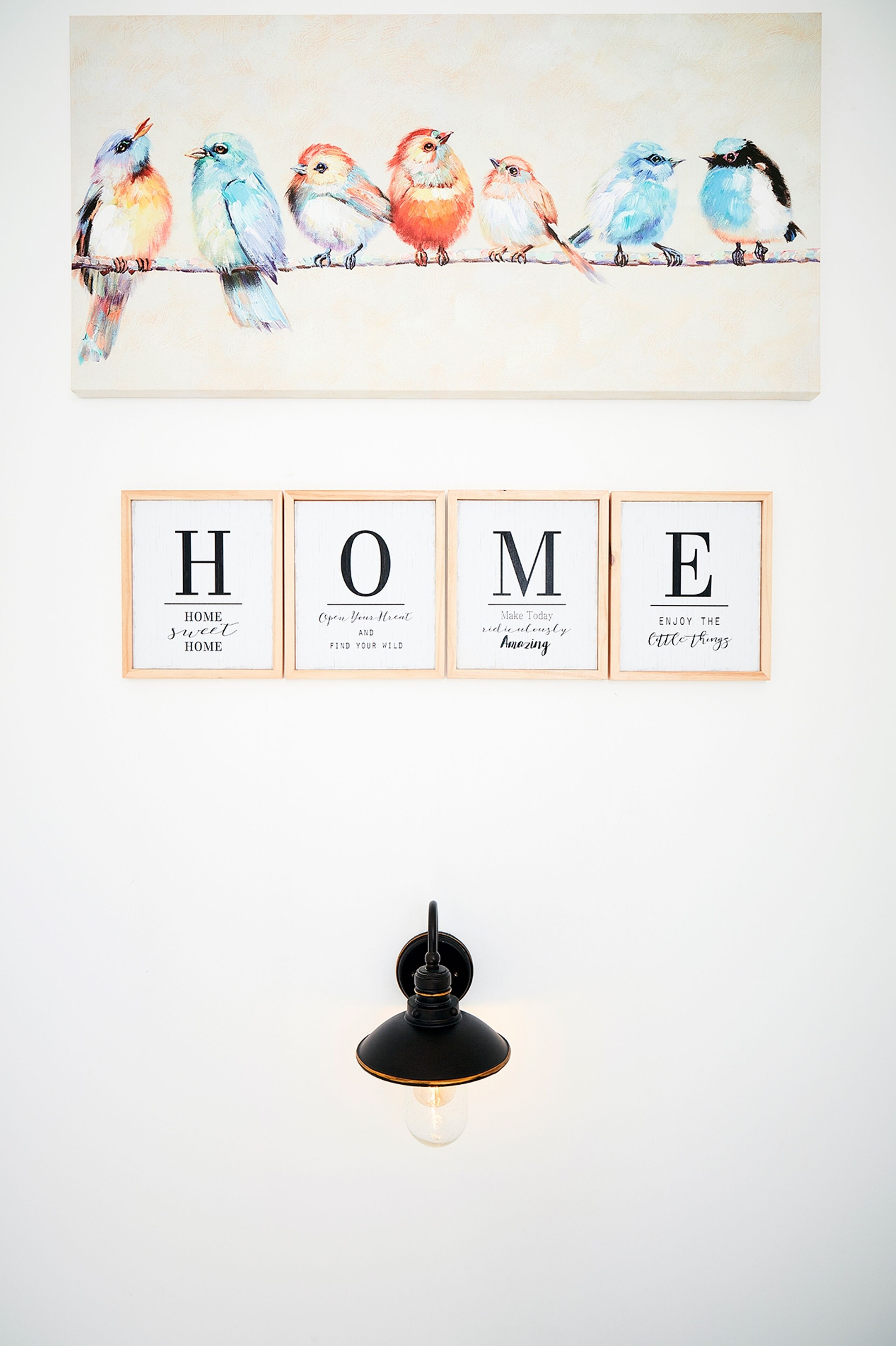 Un mur orné d’un tableau représentant des oiseaux aux couleurs vives, de citations inspirantes encadrées et d’un luminaire moderne.