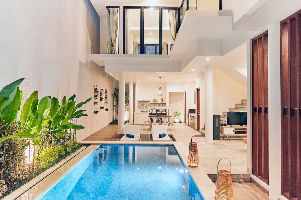 A modern indoor pool area with a kitchen and dining area in the background.
