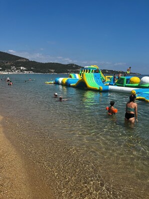 Een strand met opblaasbare waterglijbanen en helder ondiep water.