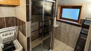 Eine kompakte Küche mit Einbauofen, einer Duschkabine und einem kleinen Fenster.