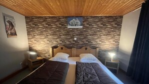 Ein Doppelbett mit zwei Kissen, ein Holz-Kopfstück, eine Steinwand und ein kleiner Nachttisch mit Lampe.