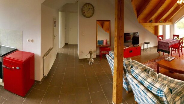 A spacious kitchen with a red refrigerator, a dining area with a red table and chairs, and a living room with a sofa and a TV. - Deosai (Kelkheim)