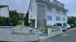 A two-story residential building with a tiled facade, a gated entrance, and parked cars. - Deosai (Kelkheim)