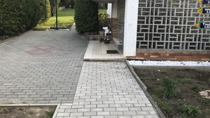 A paved driveway leading to a building with a basketball hoop, a gated entrance, and a brick wall with decorative signs. - Deosai (Kelkheim)