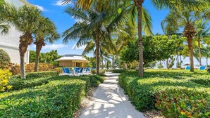 A pathway lined with palm trees and blue chairs, leading to a building with a white exterior and a covered area. - Largo Getaway • 3 King Suites + In-Laws Quarters, Pickleball (Key Largo)