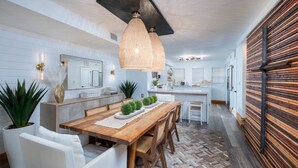 A modern kitchen with white cabinetry, a wooden dining table, and pendant lighting. - Largo Getaway • 3 King Suites + In-Laws Quarters, Pickleball (Key Largo)