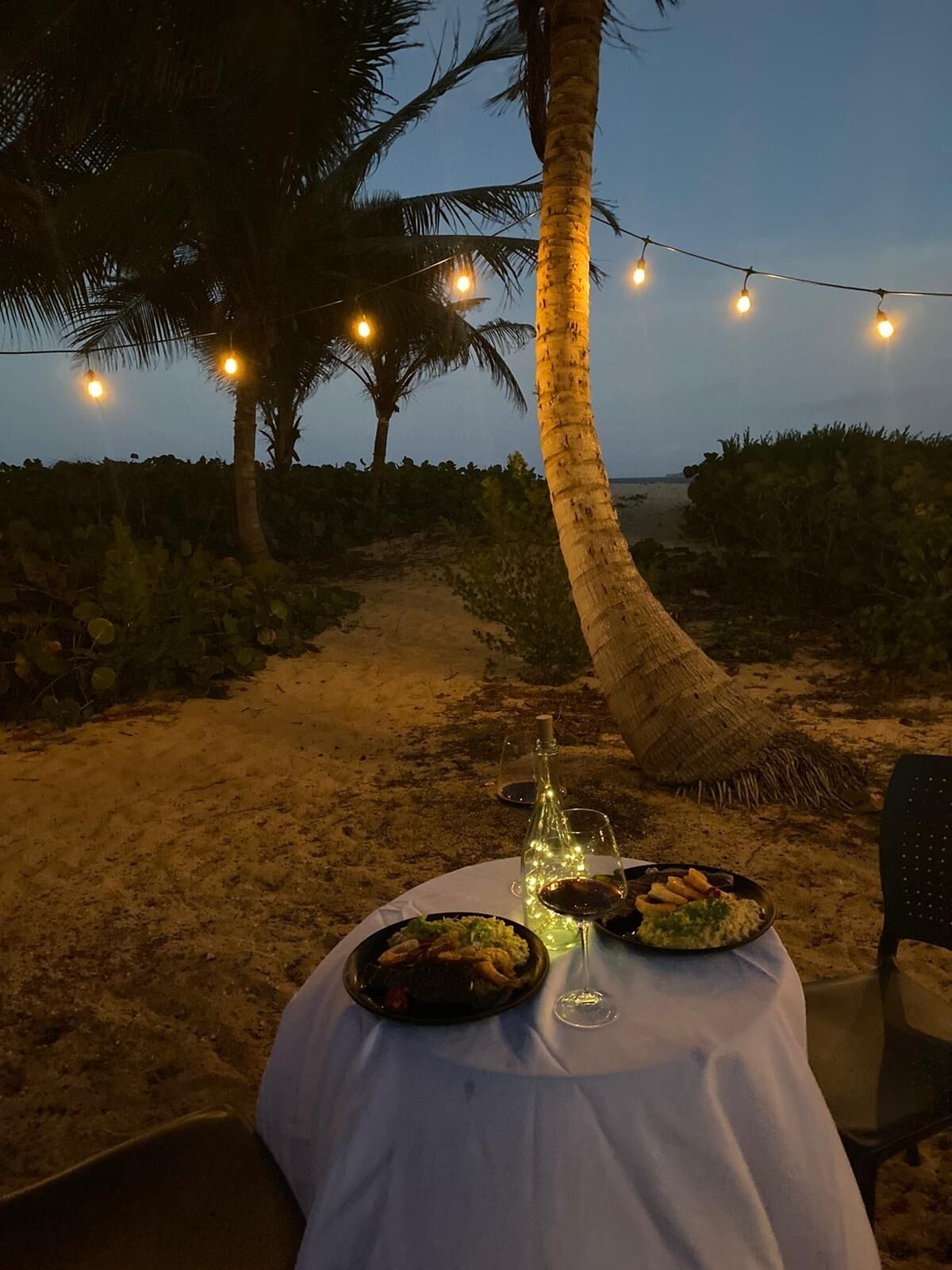 Mobiliario de comedor exterior con una mesa dispuesta para dos personas, incluyendo una botella de vino y platos de comida.