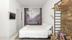 A bedroom with a bed, a TV, a wooden wardrobe, and a view of a street through a window. - Dione monolocale quiet and confortable (Syracuse)
