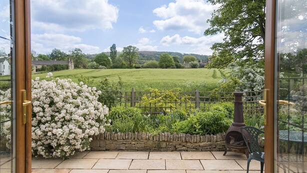 A patio with a stone wall, a metal grill, and a view of a green field and trees. - Kingfisher Cottage - sleeps 10 guests  in 5 bedrooms (Winchcombe)