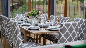 A dining table set with plates, glasses, and a vase with flowers. - Kingfisher Cottage - sleeps 10 guests  in 5 bedrooms (Winchcombe)