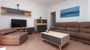 Ein modernes Wohnzimmer mit einem Flachbildfernseher, einem braunen Sofa, einem Couchtisch aus Holz und einem Gemälde eines Leuchtturms an der Wand.
