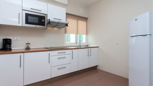 Eine kleine Küche mit weißen Schränken, einer eingebauten Mikrowelle, einer Kaffeemaschine und einem Kühlschrank.