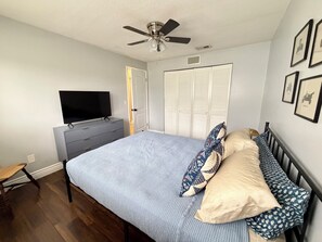 Ein Schlafzimmer mit einem Bett, einem Fernseher auf einer Kommode, einem Deckenventilator und einer Tür.