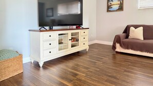A living room with a flat-screen TV mounted on a white cabinet, a brown sofa, and a framed picture on the wall. - The Oasis Private Pool Home + Best Launch Views! No cleaning fee. (Titusville)
