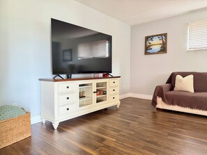Ein Wohnzimmer mit einem Flachbildfernseher an einem weißen Schrank, einem braunen Sofa und einem gerahmten Bild an der Wand.